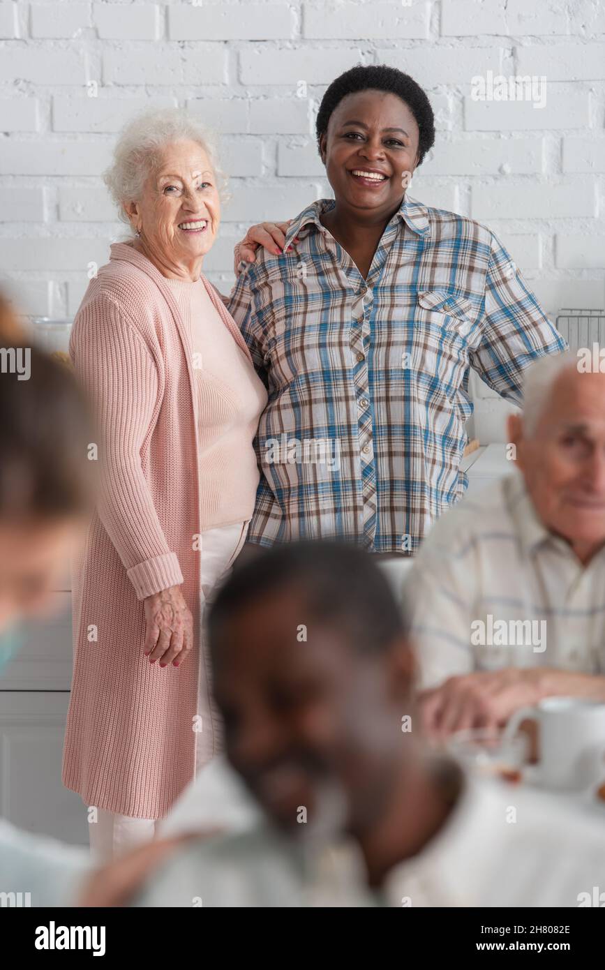Donna sorridente in piedi vicino ad un amico afroamericano in casa di cura Foto Stock