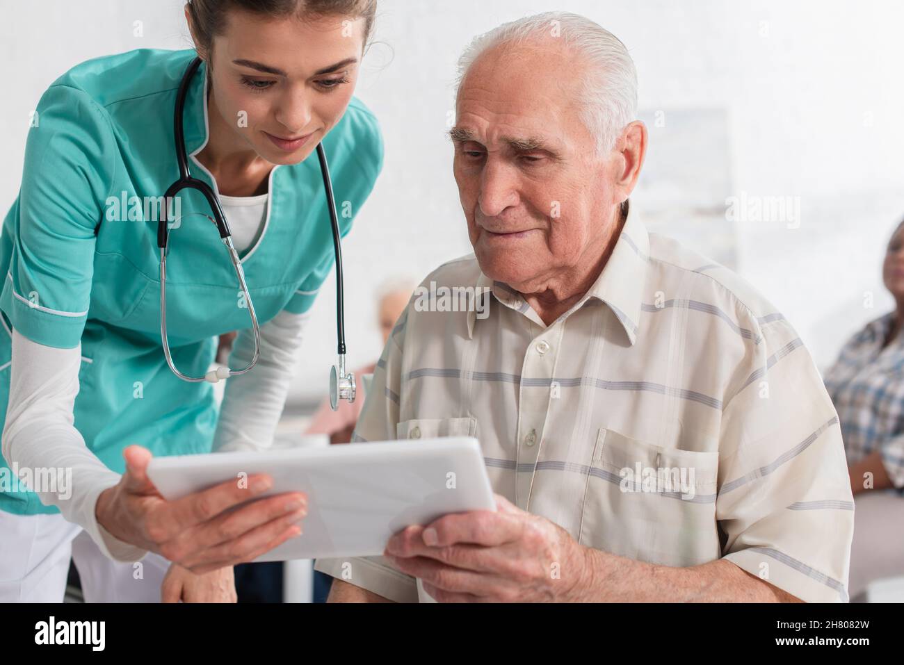 Giovane infermiere che tiene un tablet digitale vicino al paziente anziano in una casa di cura Foto Stock