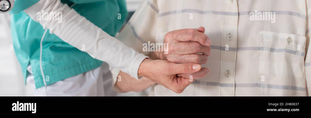 Vista ritagliata dell'infermiera giovane che tiene la mano del paziente anziano in casa di cura, banner Foto Stock