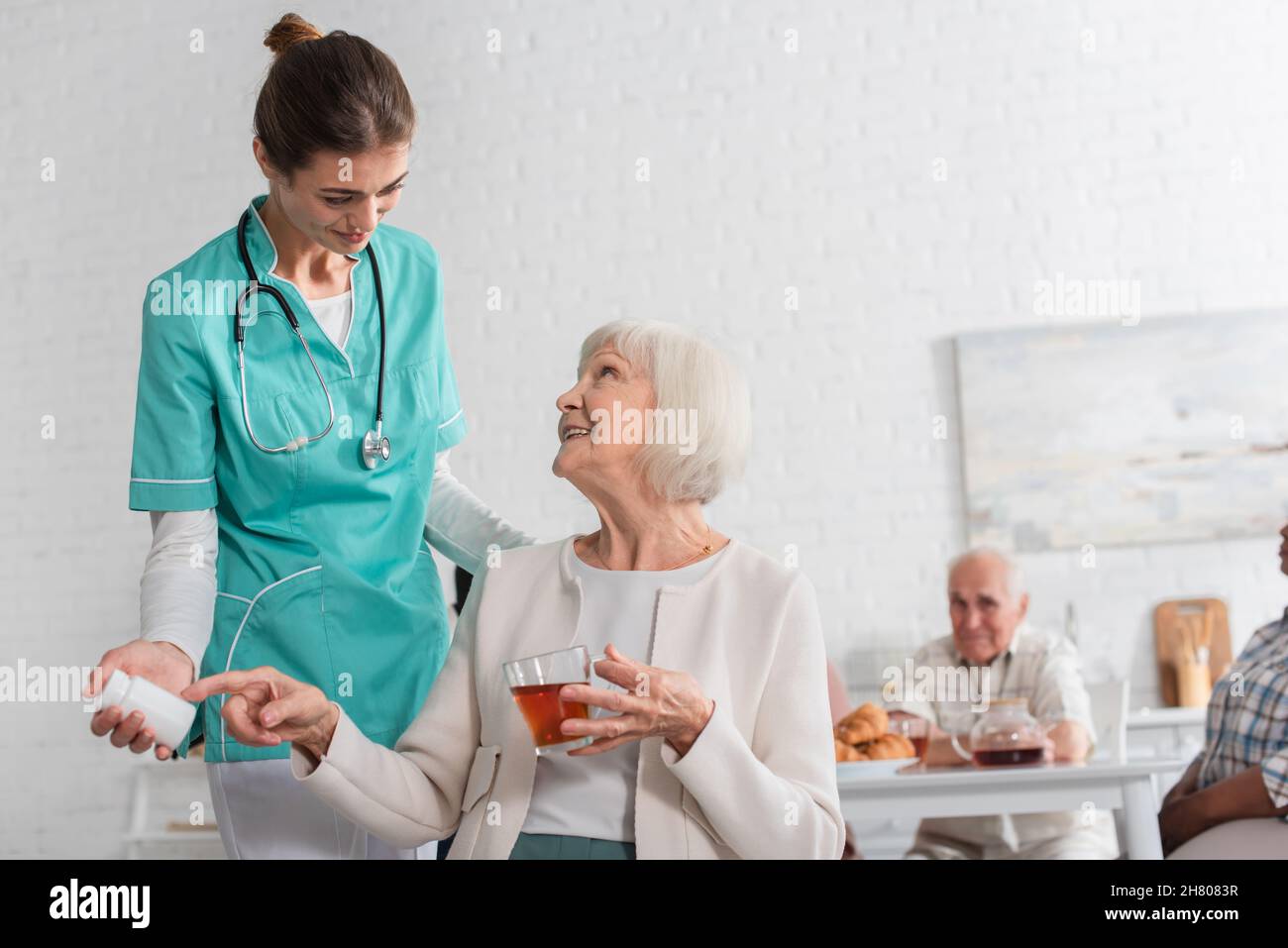 Sorridendo il paziente puntando verso le pillole e tenendo il tè vicino all'infermiere in casa di cura Foto Stock