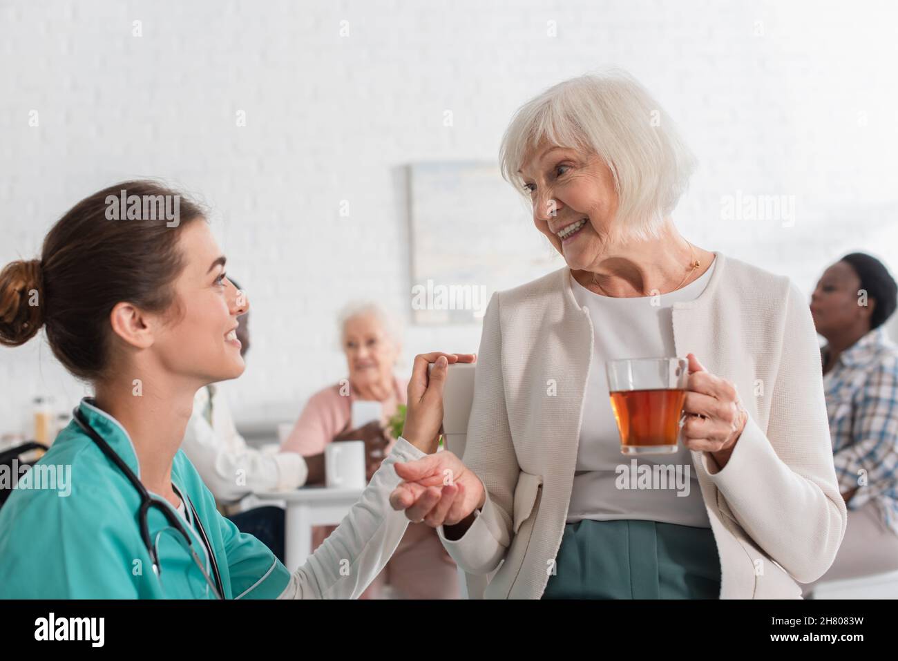 Infermiera sorridente che guarda il paziente con il tè in casa di cura Foto Stock