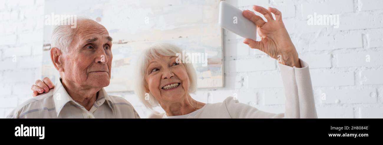 Persone anziane sorridenti mentre prendono selfie in casa di cura, banner Foto Stock