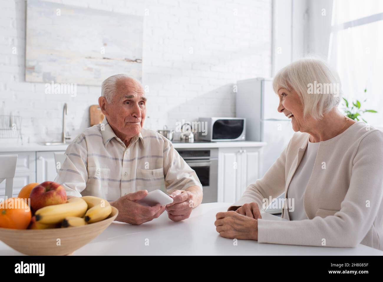 Sorridente donna anziana che guarda un amico con smartphone in casa di cura Foto Stock