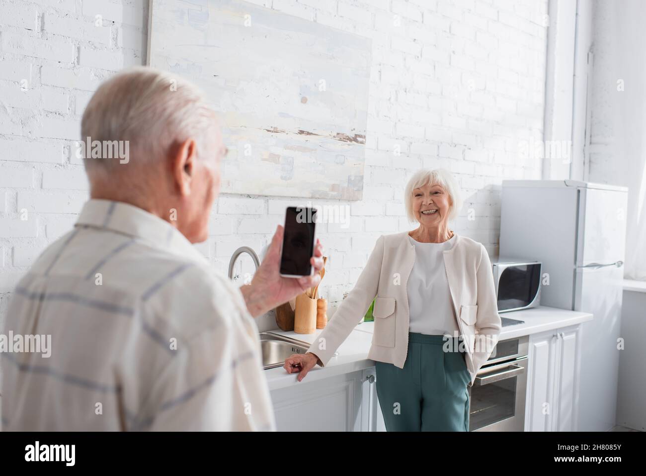Donna anziana sorridente che guarda un amico sfocato con smartphone in casa di cura Foto Stock