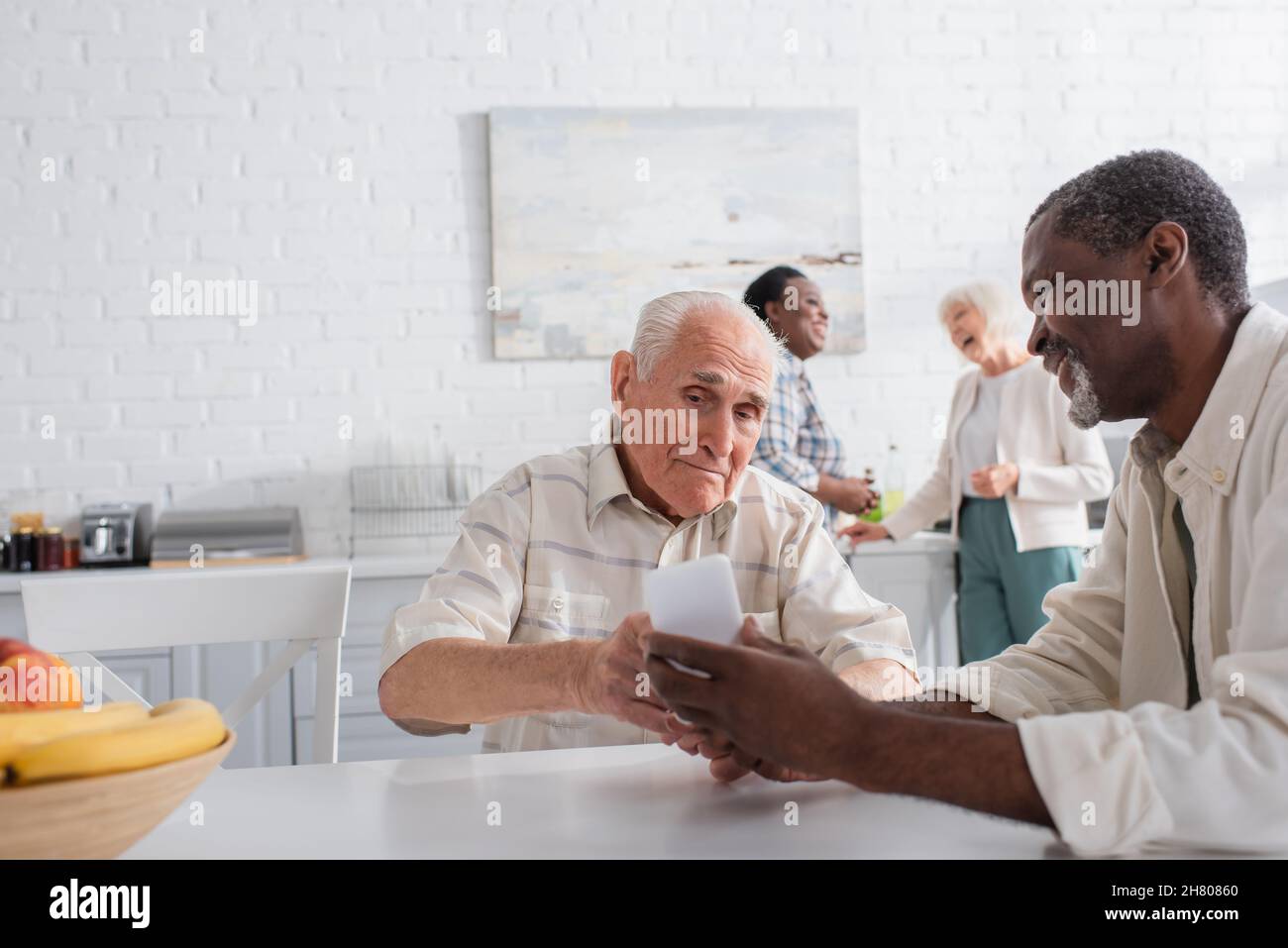Uomo afro-americano che mostra smartphone ad un amico senior vicino frutta in casa di cura Foto Stock