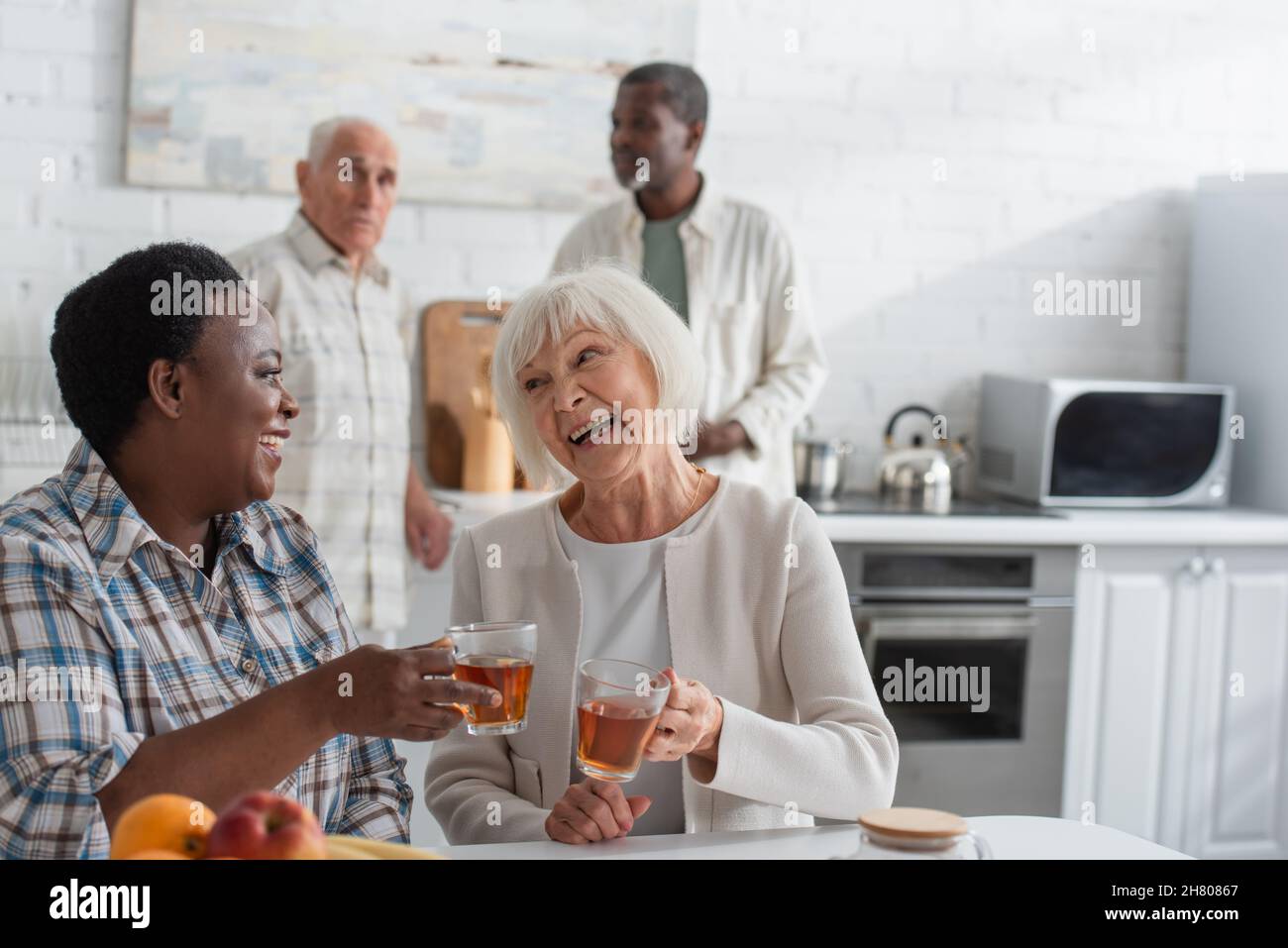 Donne interracial anziane felici che tengono il tè vicino alla frutta nella casa di cura Foto Stock