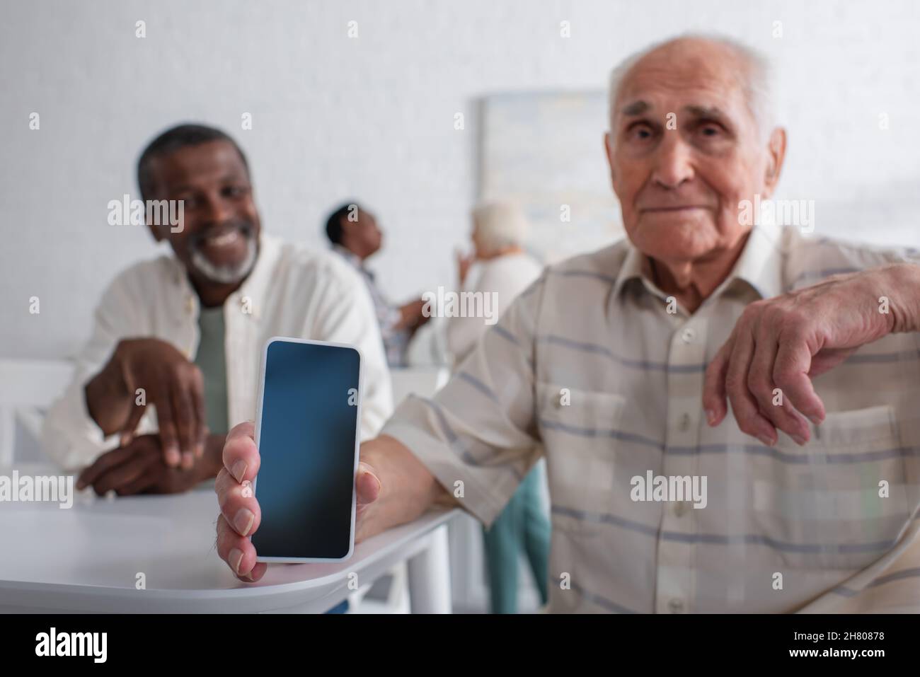 Smartphone in mano di uomo anziano offuscato vicino ad un amico afroamericano in casa di cura Foto Stock