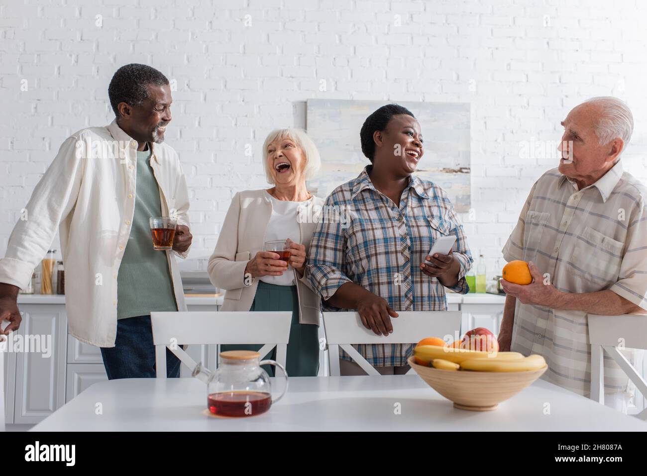 Gente multietnica allegra che tiene il tè e lo smartphone mentre parla nella casa di cura Foto Stock