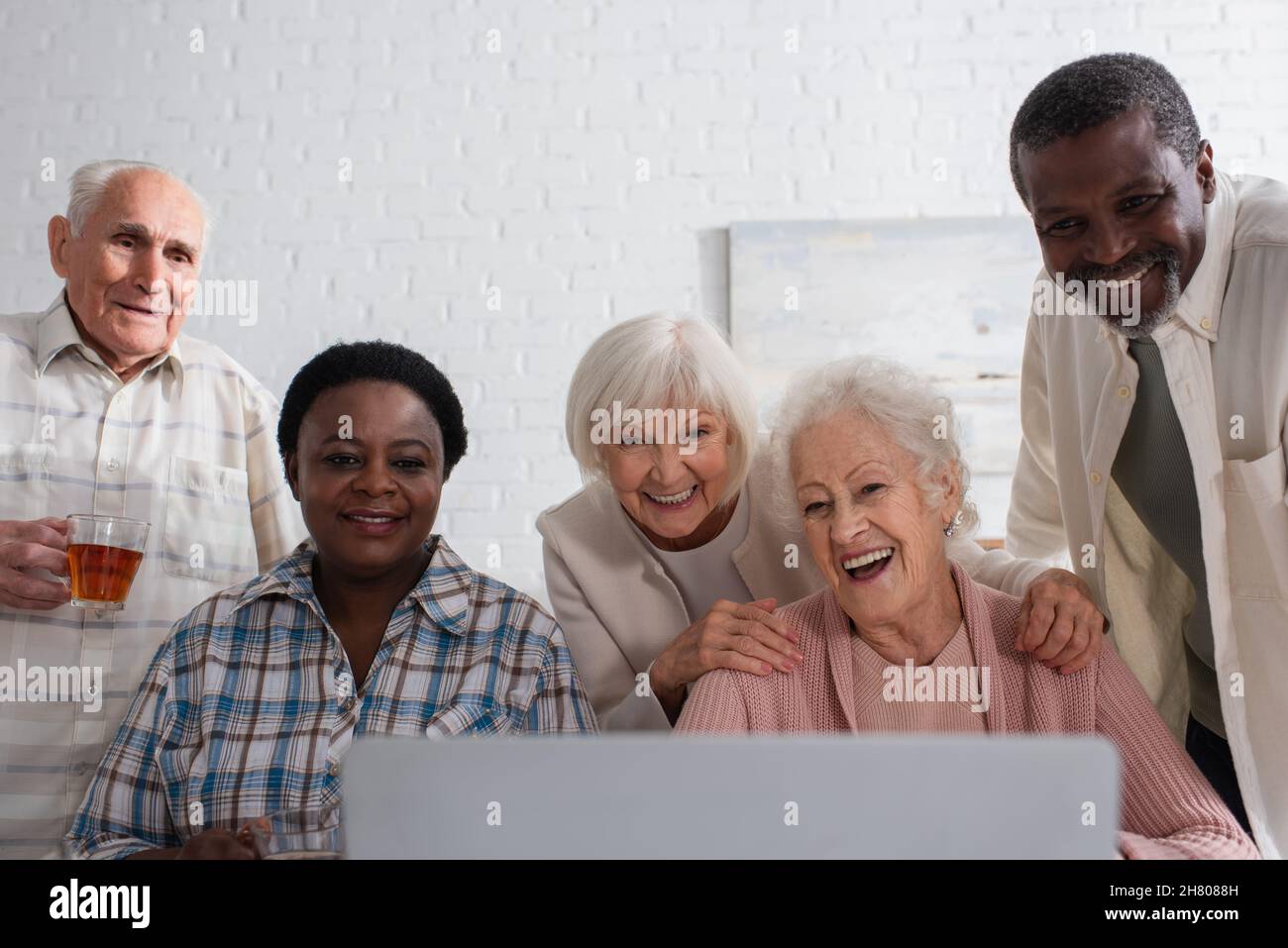 Persone anziane multietniche con tè che guardano il laptop in casa di cura Foto Stock
