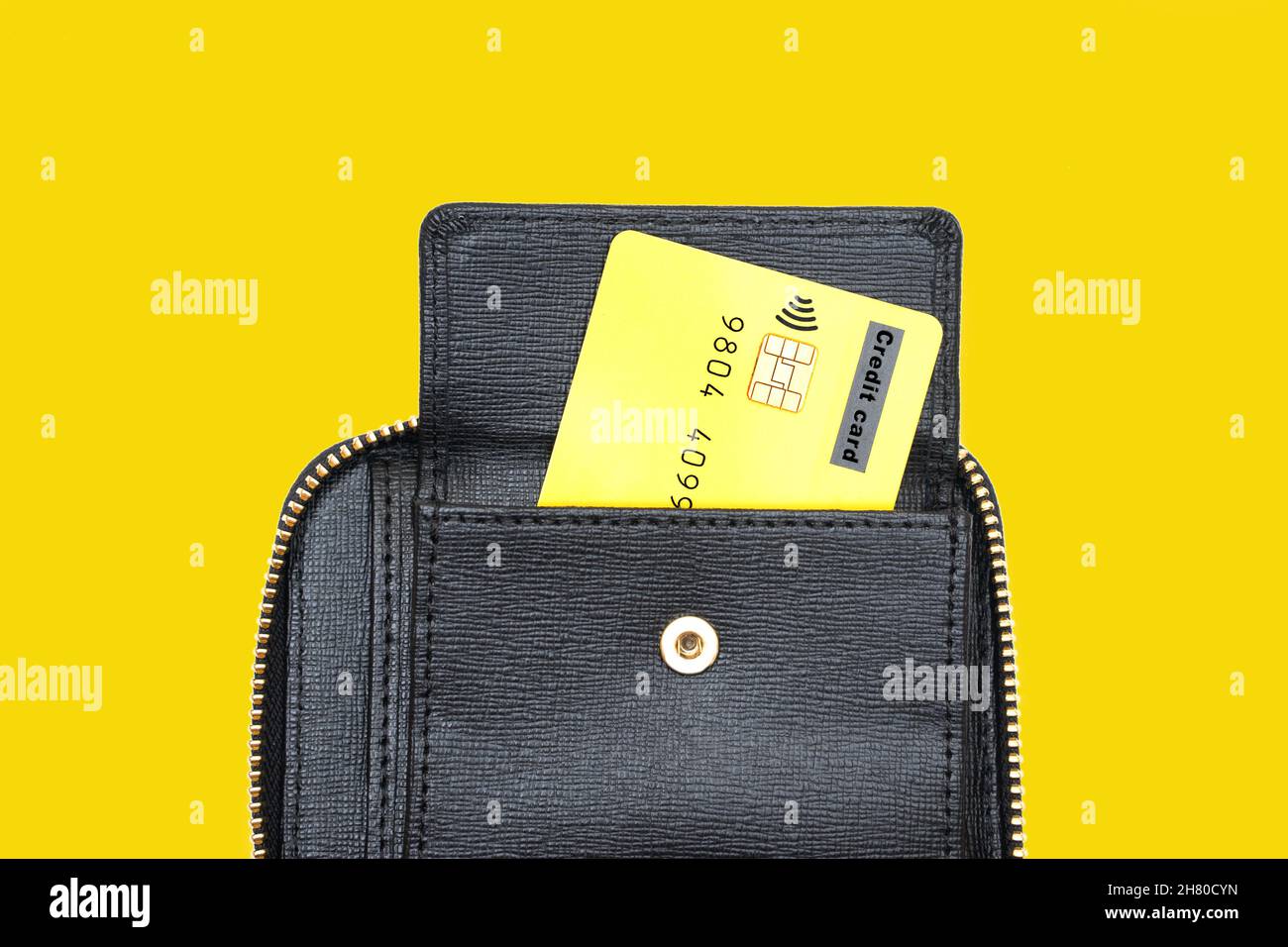 Carta di credito che sporge da una chiusura a cerniera nera a portafoglio isolato su sfondo giallo. Foto Stock