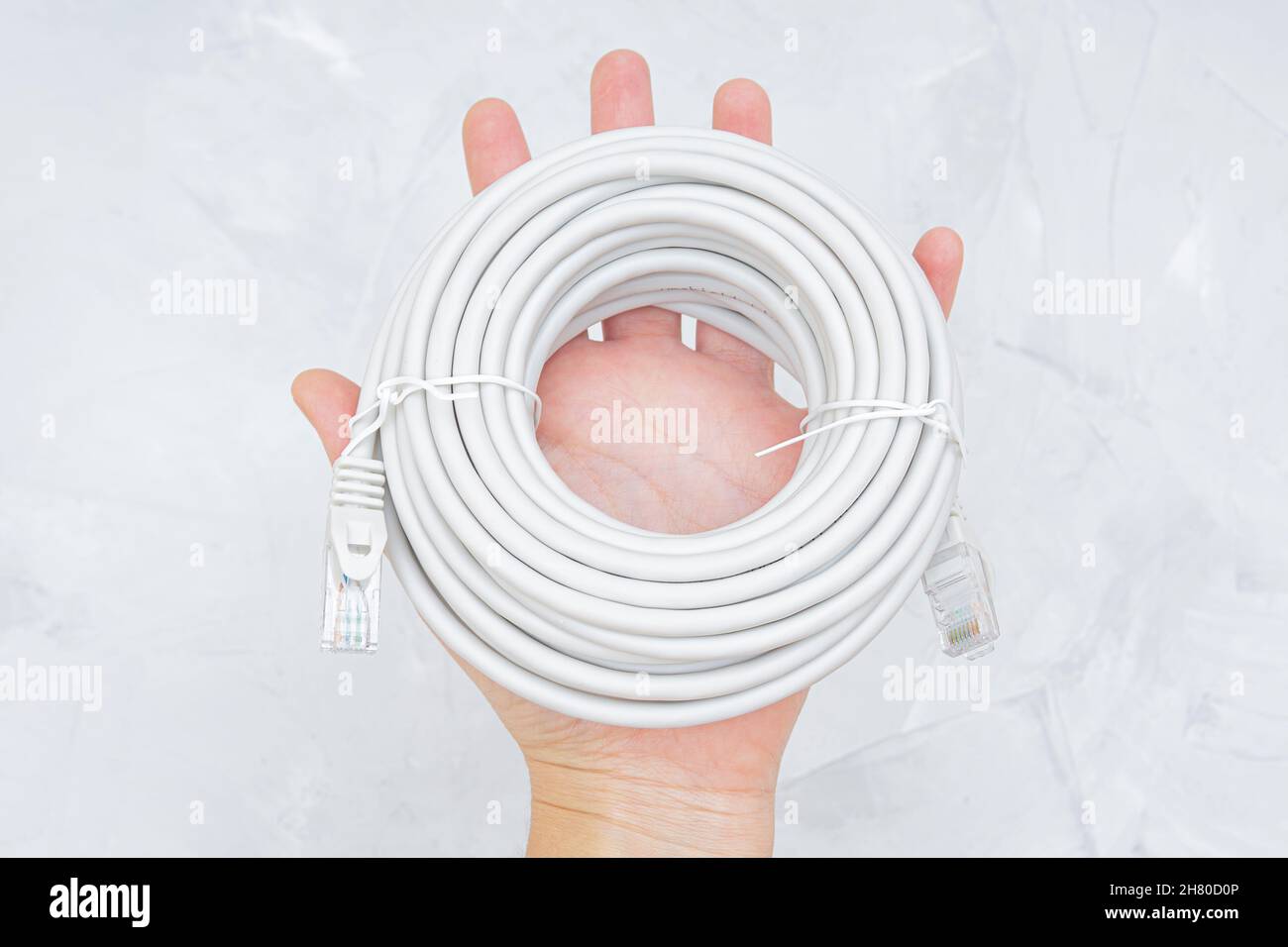 Rotolo di cavo ethernet in mano su sfondo grigio. Foto Stock