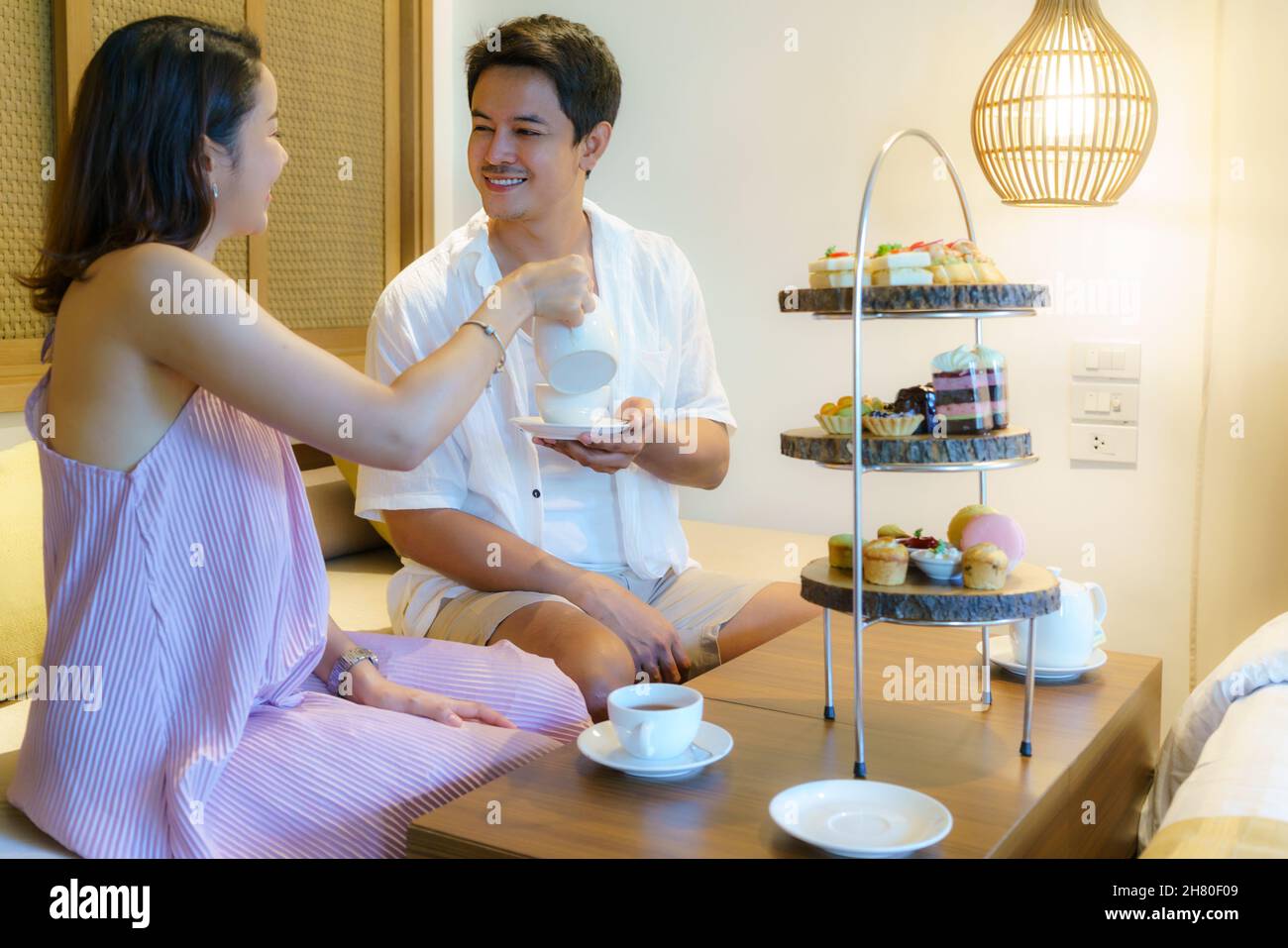 Le coppie asiatiche stanno godendo una vacanza romantica. Avendo un tè pomeridiano impostato come una donna versa il tè per il suo ragazzo in una lussuosa camera da letto dell'hotel. Foto Stock
