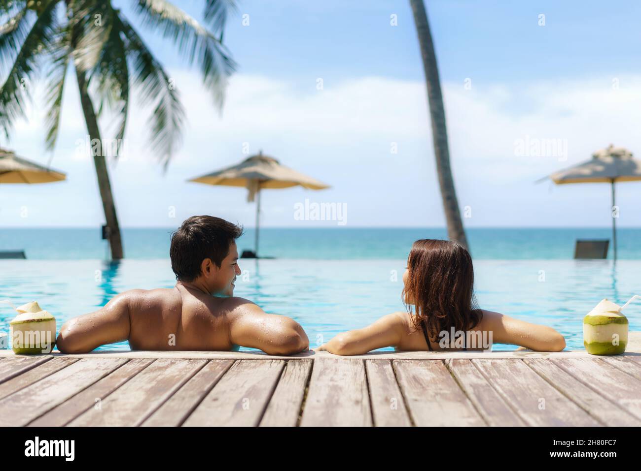 Concetto di vacanza di viaggio d'estate, viaggiatore asian coppia con cocco relax nel lussuoso resort a sfioro con piscina, spiaggia di mare e sfondo di palme Foto Stock