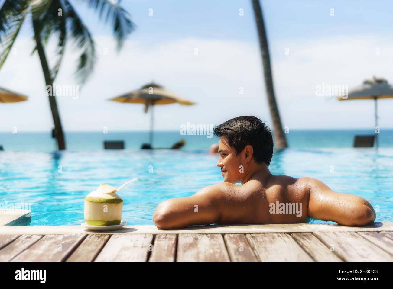 Concetto di vacanza di viaggio d'estate, viaggiatore asiatico uomo con cocco relax nel lussuoso resort a sfioro piscina hotel con spiaggia di mare e palme sfondo Foto Stock