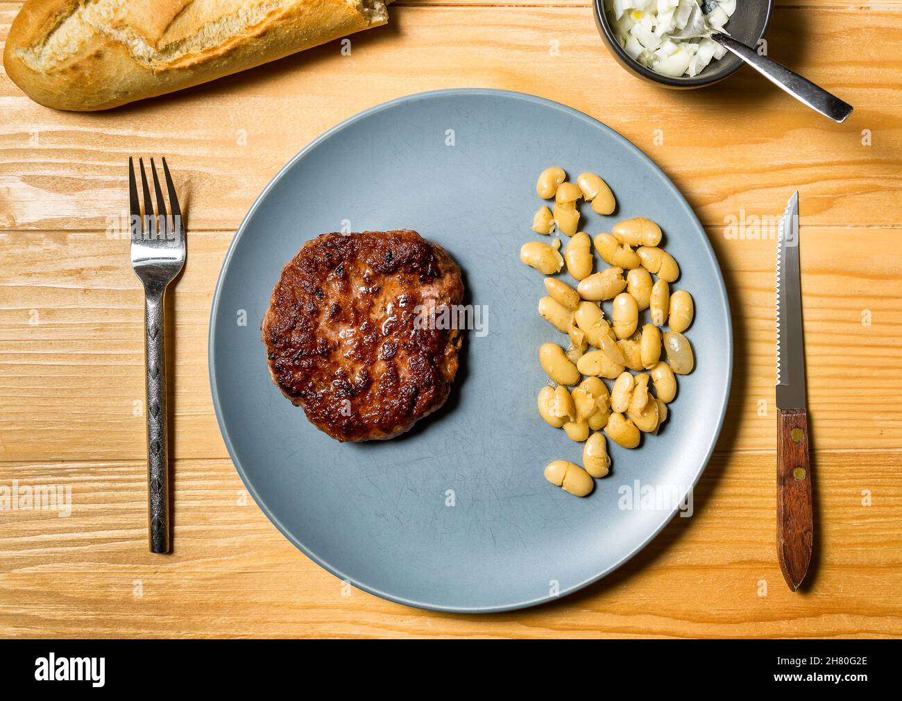 Gustoso hamburger alla griglia servito con fagioli vegetariani cotti in un piatto su un rustico tavolo di legno. Disposizione piatta, vista dall'alto Foto Stock