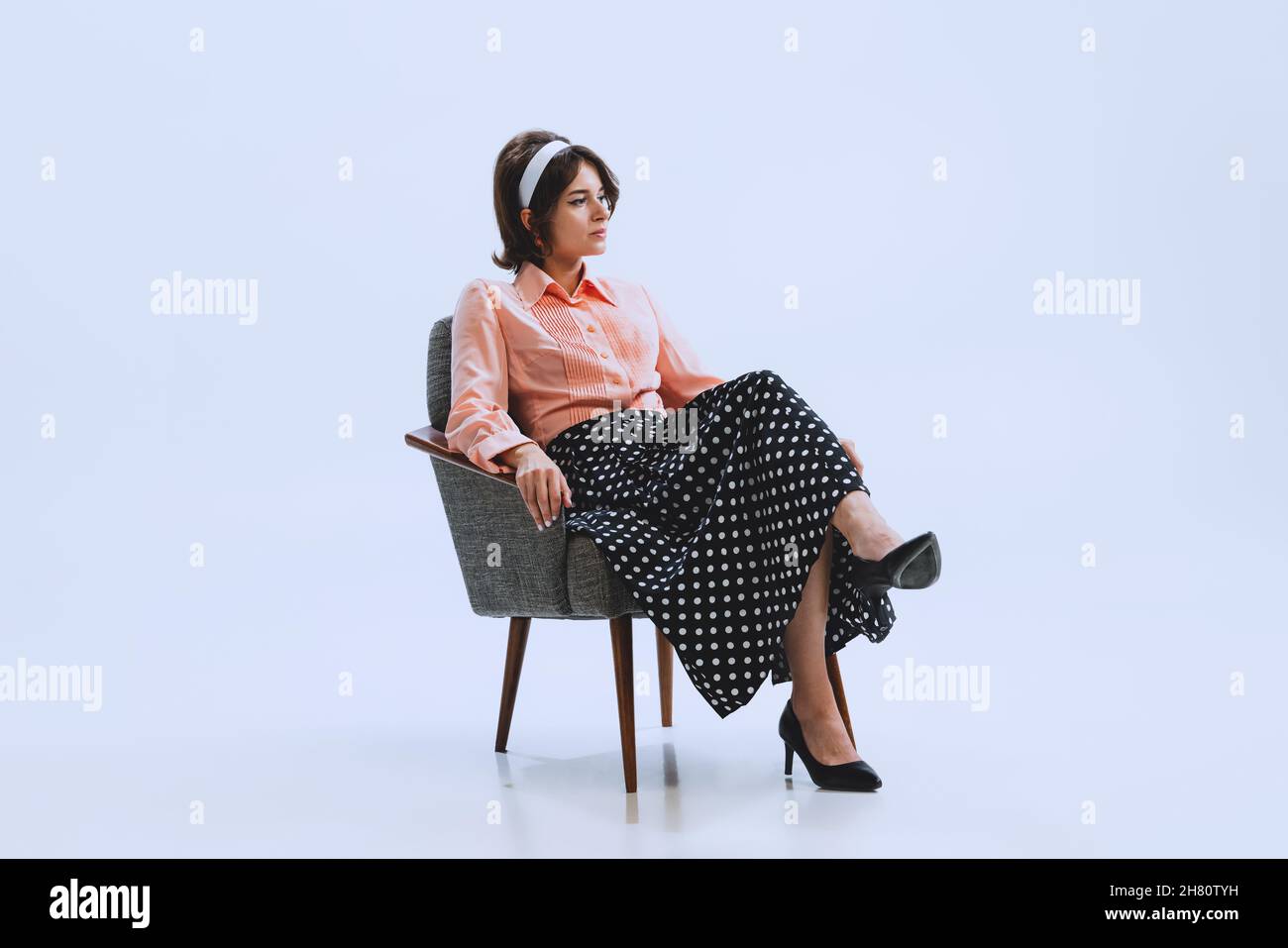 Ritratto di giovane ragazza triste in stile retrò, moda degli anni '70, sessanta anni seduta in sedia isolato su sfondo bianco studio con copyspace per l'annuncio. Foto Stock