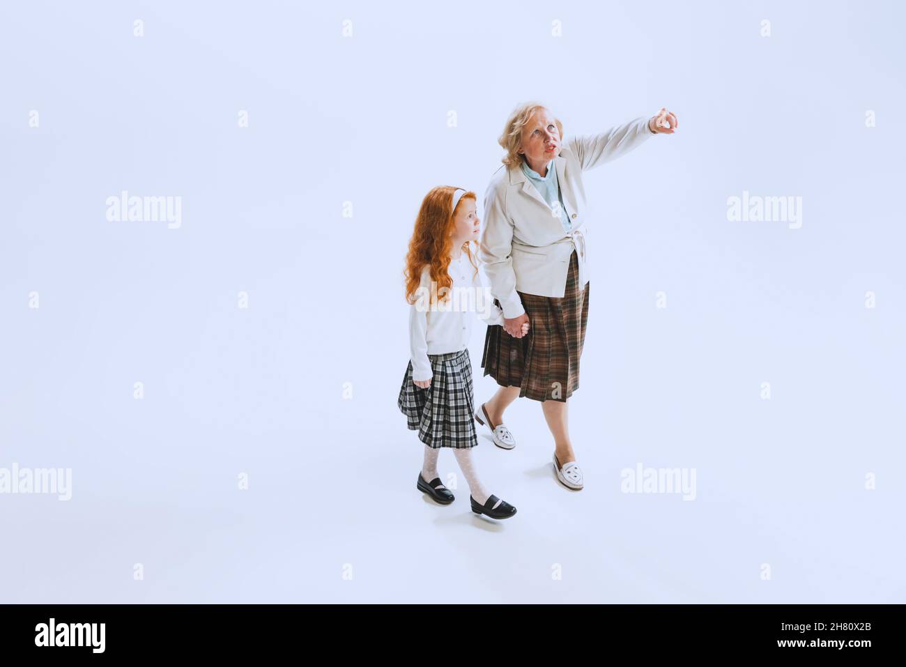 Due persone, bambina e donna anziana in stile retrò abiti, moda degli anni '70, anni '60 camminare insieme isolato su sfondo bianco studio Foto Stock