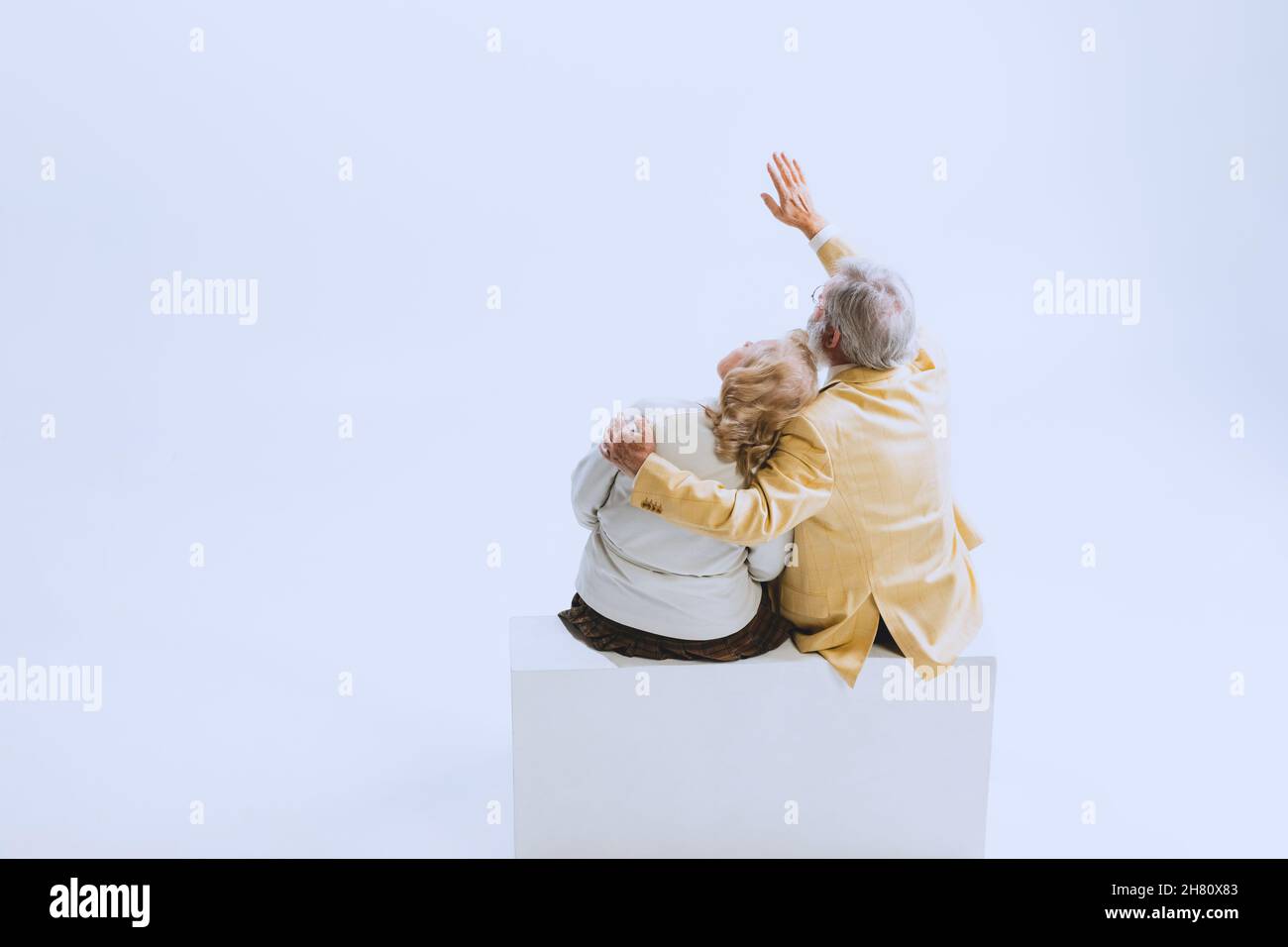 Vista posteriore di due persone, donna anziana e uomo in stile retrò abiti, moda degli anni '70, anni '60 seduti insieme isolato su studio bianco Foto Stock