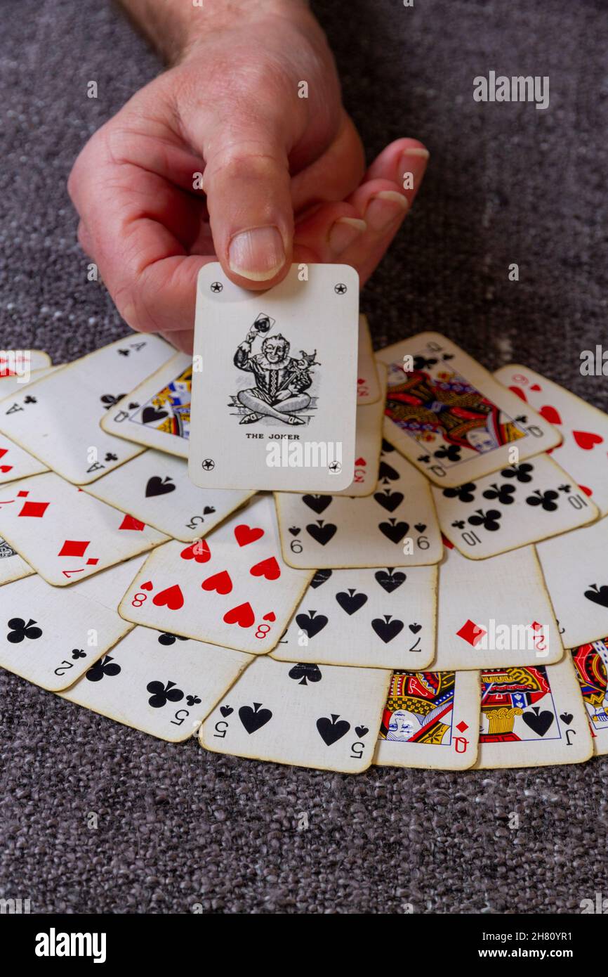 Una mano che tiene fuori un burlone che gioca le carte sopra splicato che gioca le carte Foto Stock