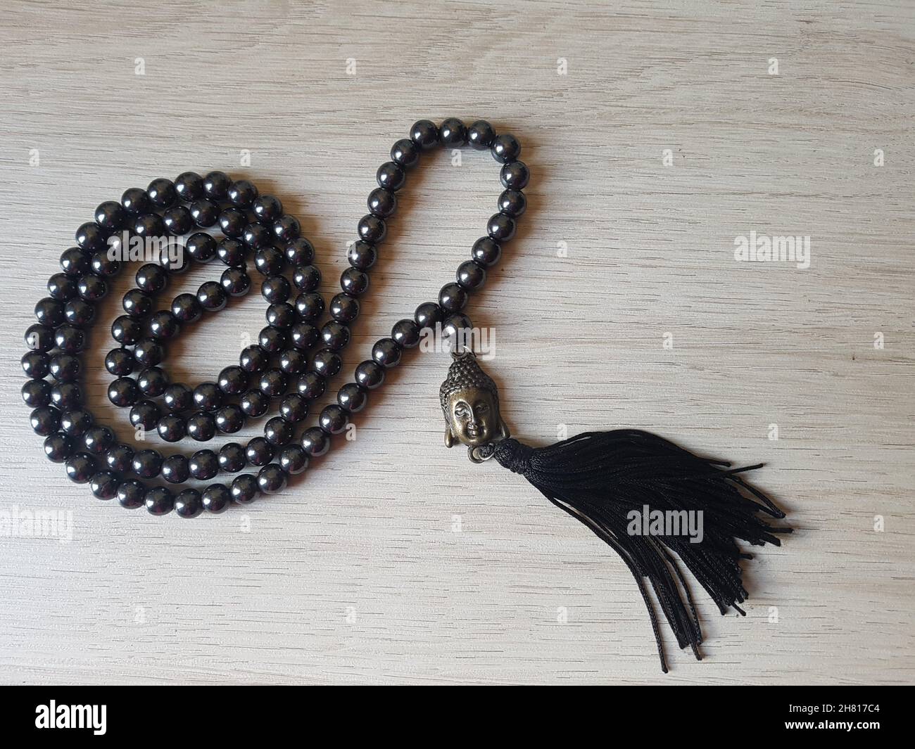 Japamala o Japa Mala, cordoncino di 108 perle di ematite e un pendente con la faccia di un Buddha, su un tavolo di legno. Foto Stock