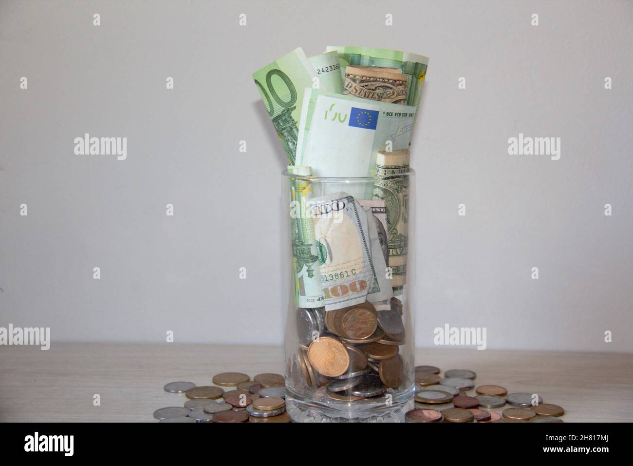 Vaso di vetro con molte banconote in euro, dollari e monete. Su un tavolo di legno. Foto Stock