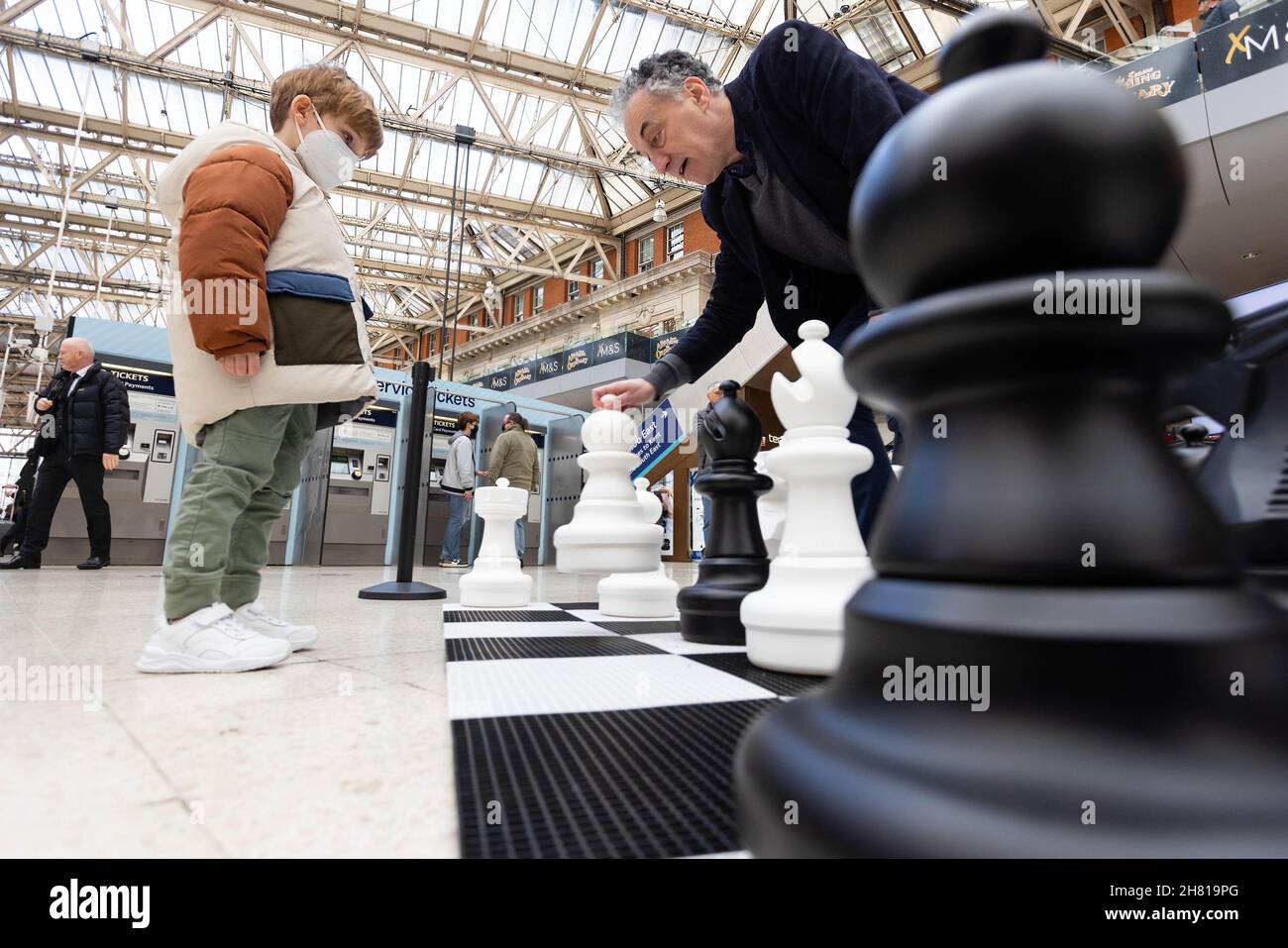 SOLO PER USO EDITORIALE (da sinistra a destra) Miles Leonard Walker, di 5 anni gioca una partita di scacchi con Malcolm Pein International Master e corrispondente di scacchi del Daily Telegraph su una scacchiera gigante presso la stazione di Waterloo a Londra, durante il live-stream dell'annuale FIDE Chess World Championship, Come campione del mondo Magnus Carlsen compete contro lo sfidante Ian Nepomniachtchi per un fondo premio di 2 milioni di euro a Dubai. Data foto: Venerdì 26 novembre 2021. Foto Stock