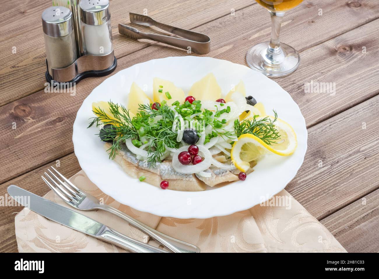 Aringhe con patate, cipolle e aneto su un piatto bianco su sfondo di legno scuro Foto Stock