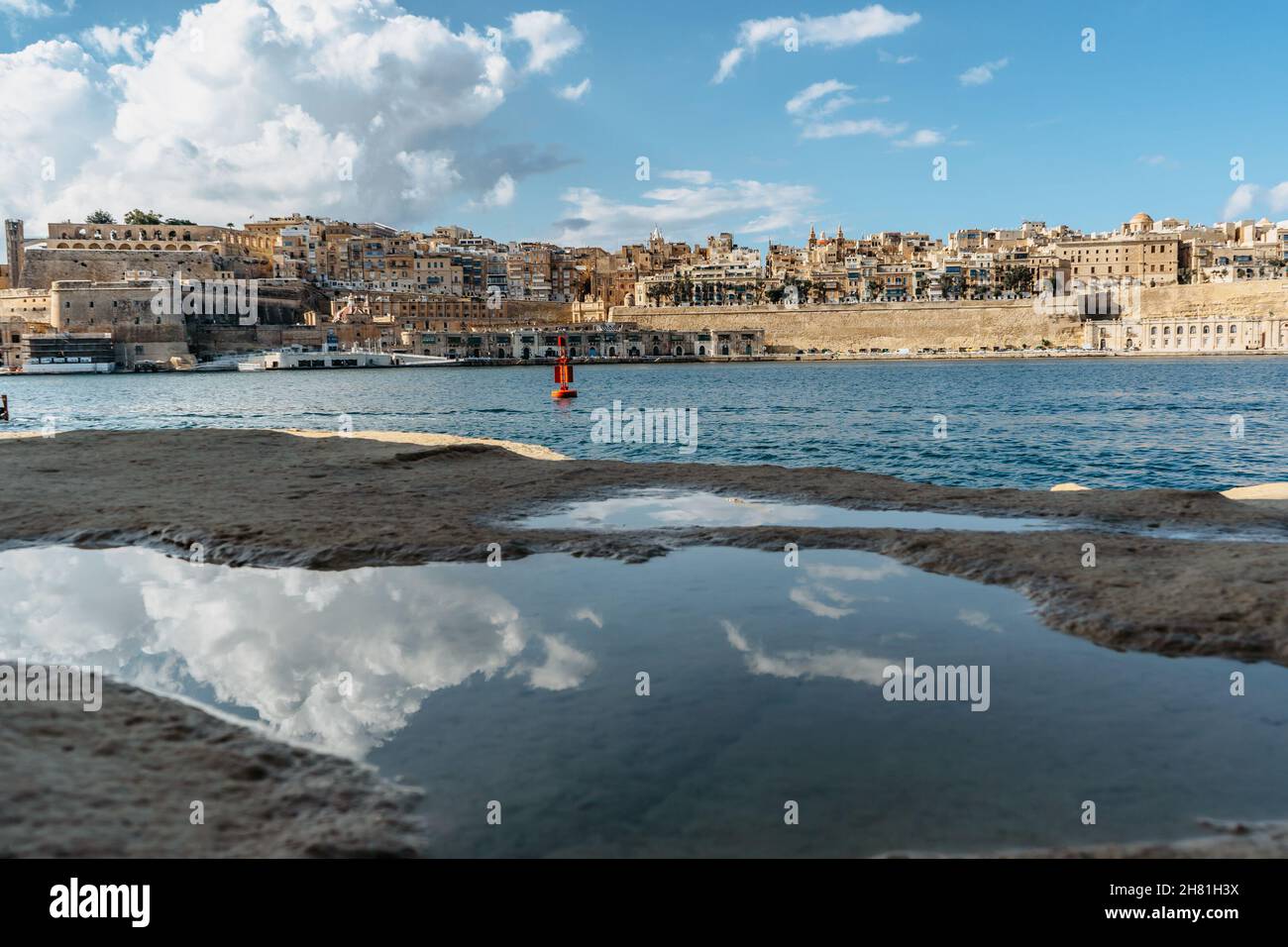 Vista panoramica della Valletta, Malta. Skyline della città dal porto di Birgu Vittoriosa. Paesaggio urbano tranquillo, giorno d'estate soleggiato, nuvole riflesse nell'acqua. Waterfront Foto Stock