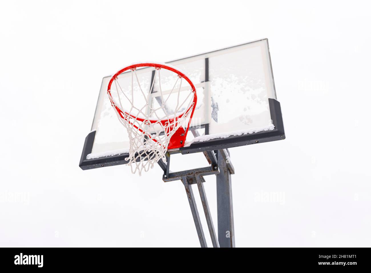 Cerchio di basket rosso su una tavola posteriore su uno sfondo chiaro, vista dal basso. Attrezzature sportive per una partita di palla all'aperto di squadra. Telaio in acciaio, protezione in plexiglass. Foto Stock