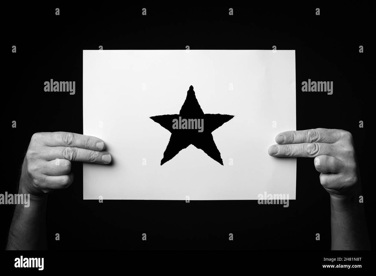 Immagine B+W delle mani maschili che tengono il foglio di carta con il simbolo della stella di natale su sfondo nero. Foto Stock