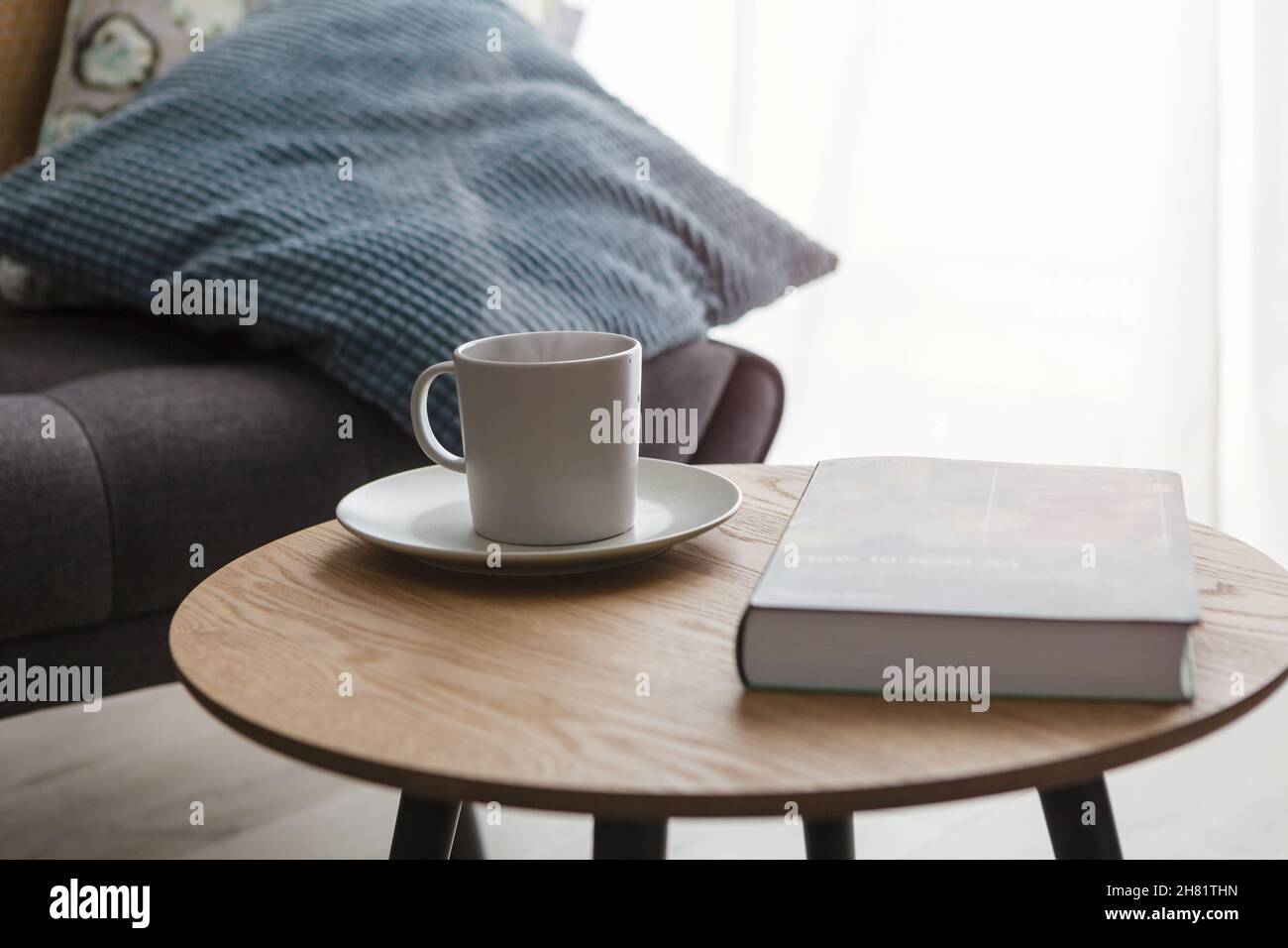 Rilassati a casa, tazza di tè caldo e prenota sul tavolino accanto al divano Foto Stock