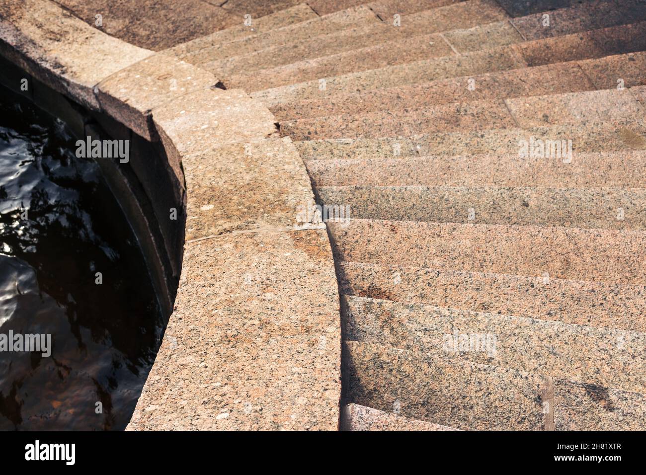 Una vecchia scalinata piegata in pietra di granito marrone scende fino all'acqua del fiume. Sfondo astratto dell'architettura. Argine del fiume Neva, San Pietroburgo, Foto Stock