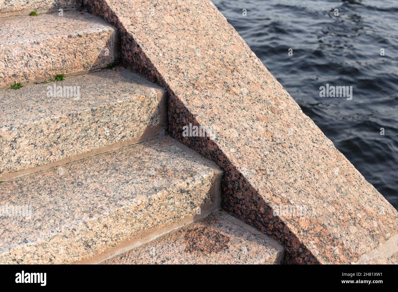 Vecchia scalinata in blocchi di pietra di granito marrone scende fino al fiume acqua, closeup foto con fuoco selettivo. Sfondo astratto dell'architettura. Ne Foto Stock