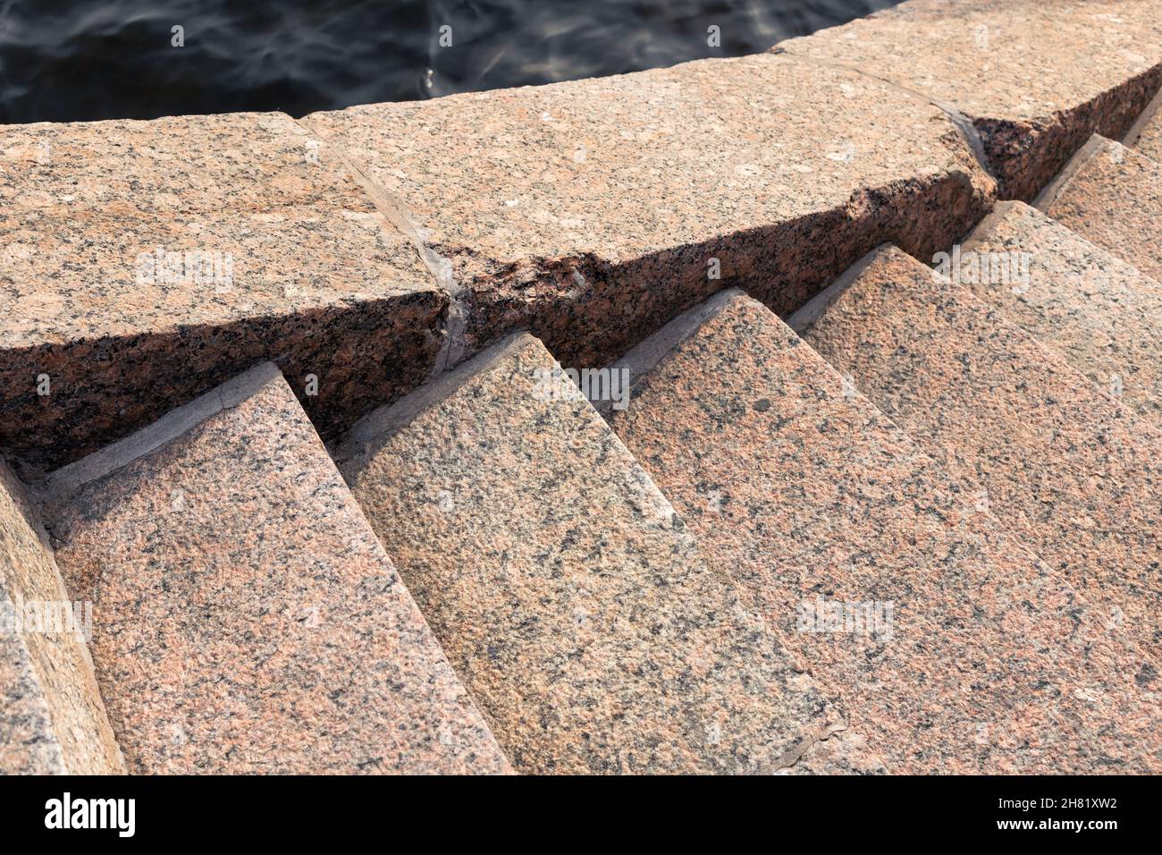 Vecchia scalinata in blocchi di pietra di granito marrone scende fino al fiume acqua, closeup foto con fuoco selettivo. Sfondo astratto dell'architettura. Ne Foto Stock
