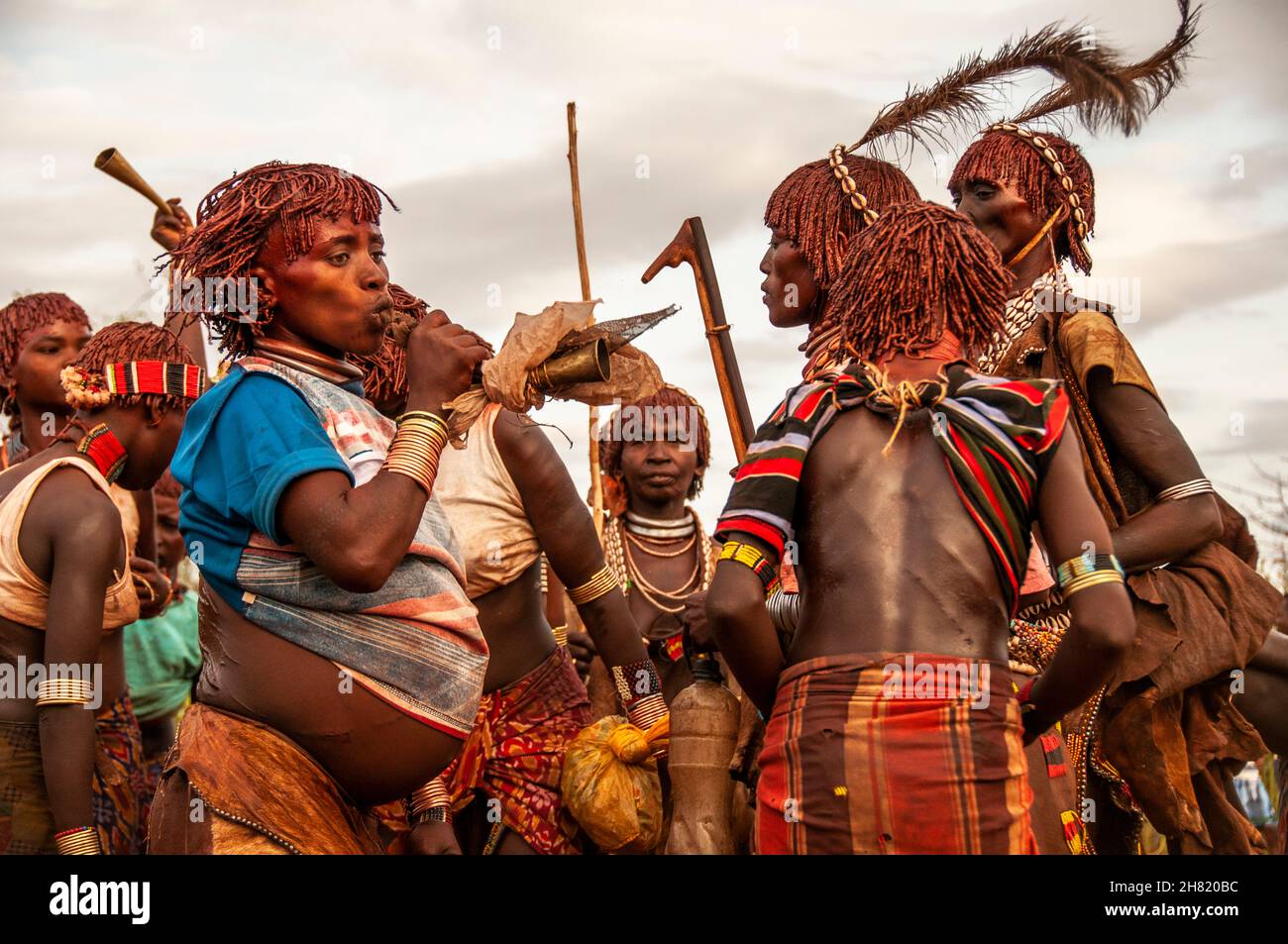 Le donne della tribù di Hamar cantano, ballano e soffiano corna per fare rumore prima dell'inizio della cerimonia di salto del toro Foto Stock