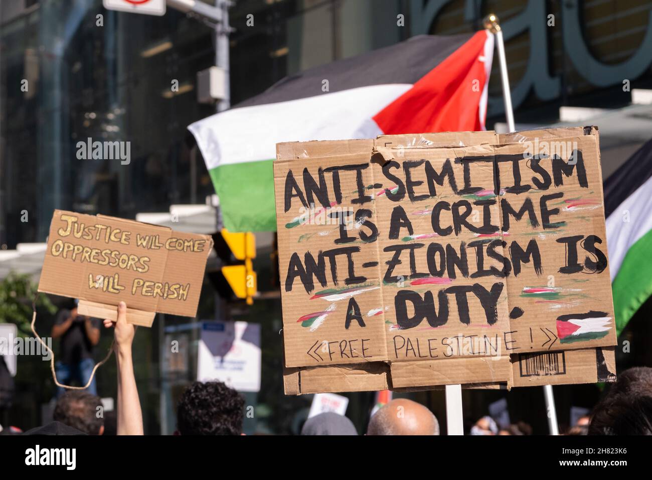 I manifestanti hanno un cartello anti-Israele e ondano bandiere palestinesi ad un evento pro-palestinese a Toronto, Ontario. Foto Stock