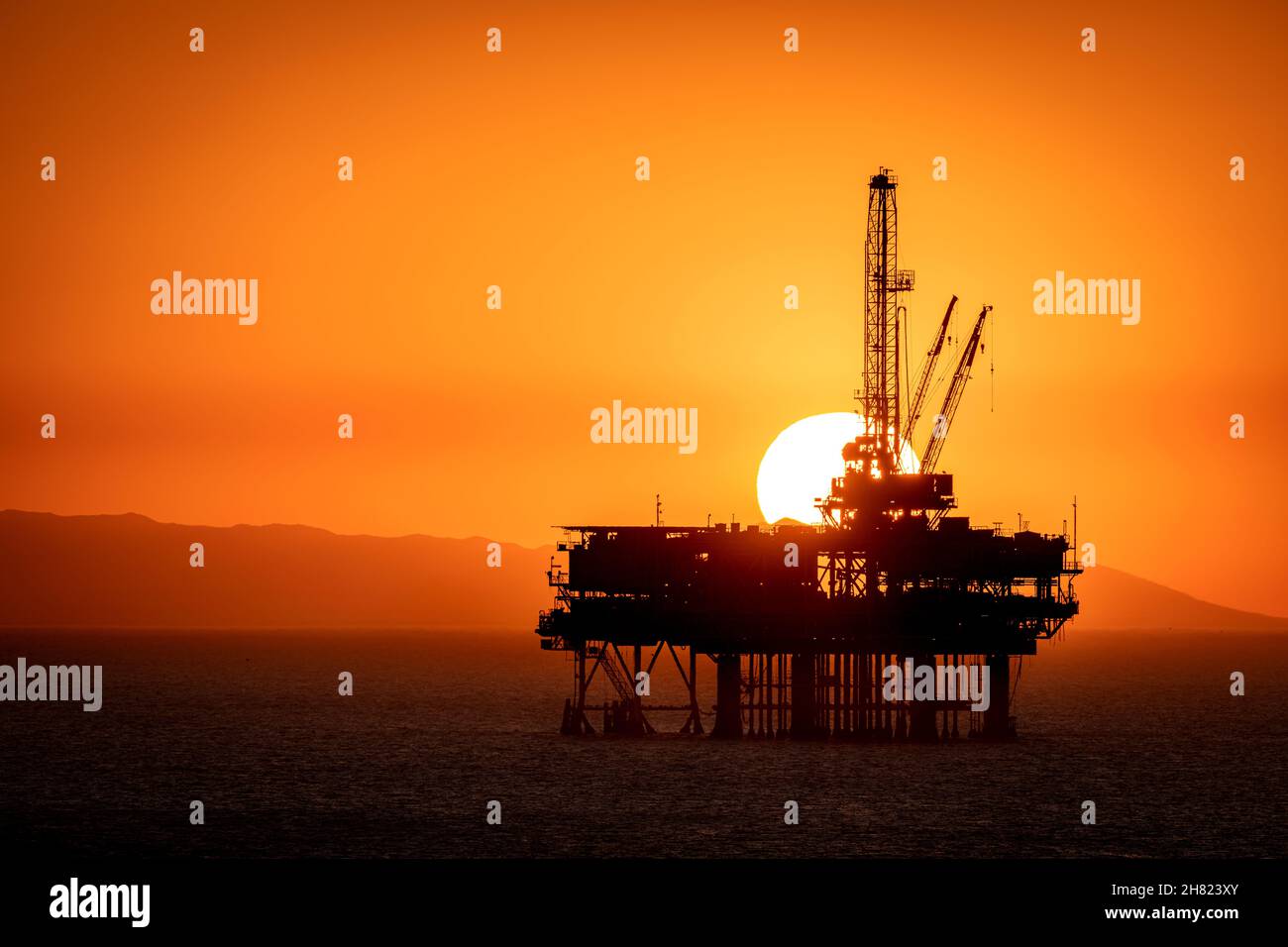 La piattaforma petrolifera offshore al largo della costa californiana si staglia contro un cielo arancione pieno di fumo da un vicino incendio mentre il sole tramonta dietro il carro. Foto Stock