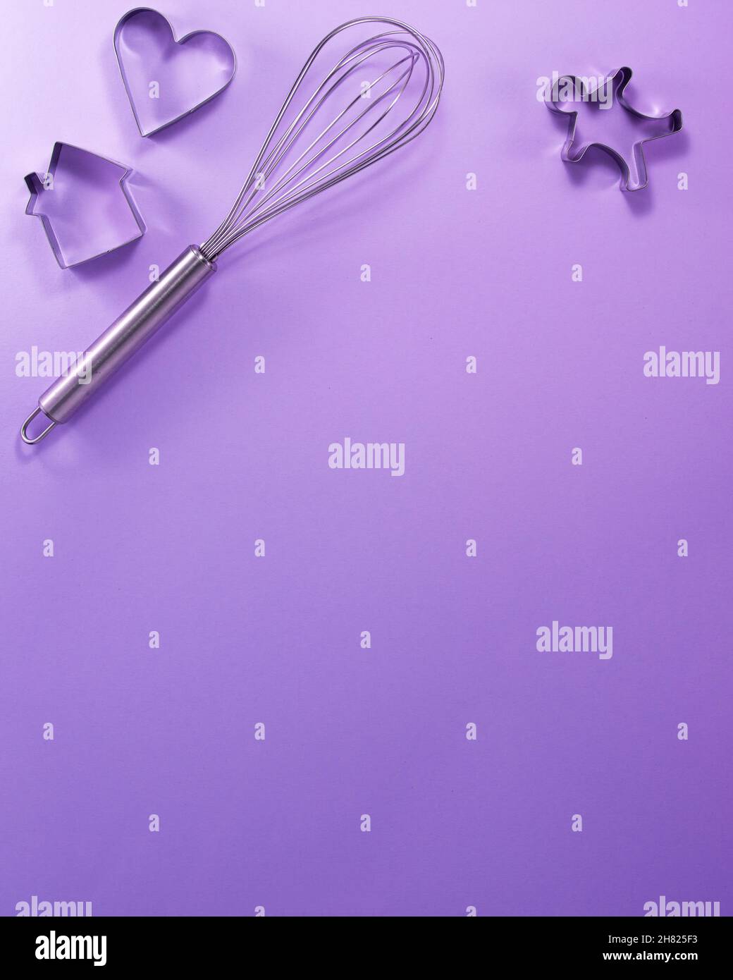Acciaio whisk casa uomini e cuore a forma di taglierina piatta posare vista dall'alto. Concetto di cucina dolciaria con spazio di copia su sfondo di carta viola brillante. Nati Foto Stock