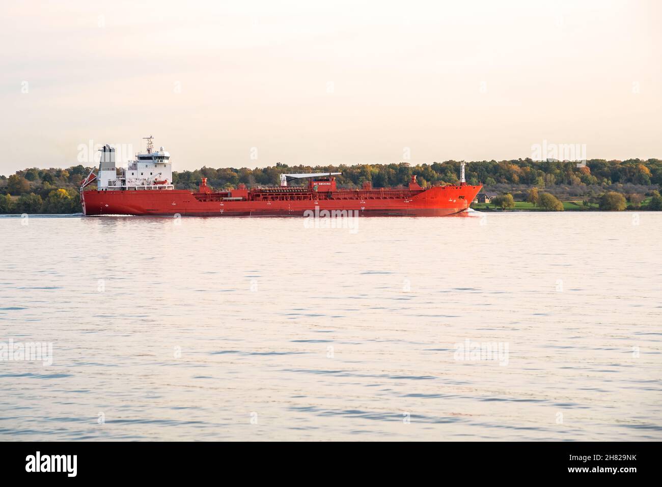 Petroliera chimica in navigazione su un lago al tramonto in autunno. Un'isola boscosa è sullo sfondo. Foto Stock