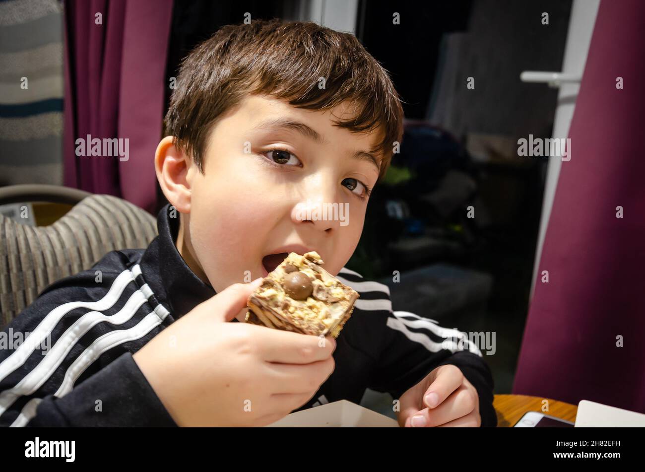 Un ragazzo che mangia un pezzo di tiffin, un dolcetto al cioccolato fatto con cioccolato e biscotti schiacciati. Foto Stock