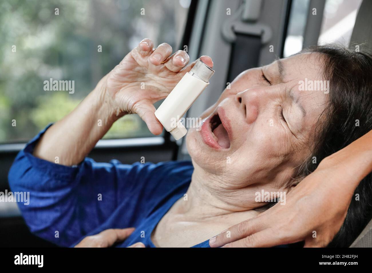 Donna anziana soffocante e che tiene uno spray per l'asma all'interno dell'auto sulla strada Foto Stock