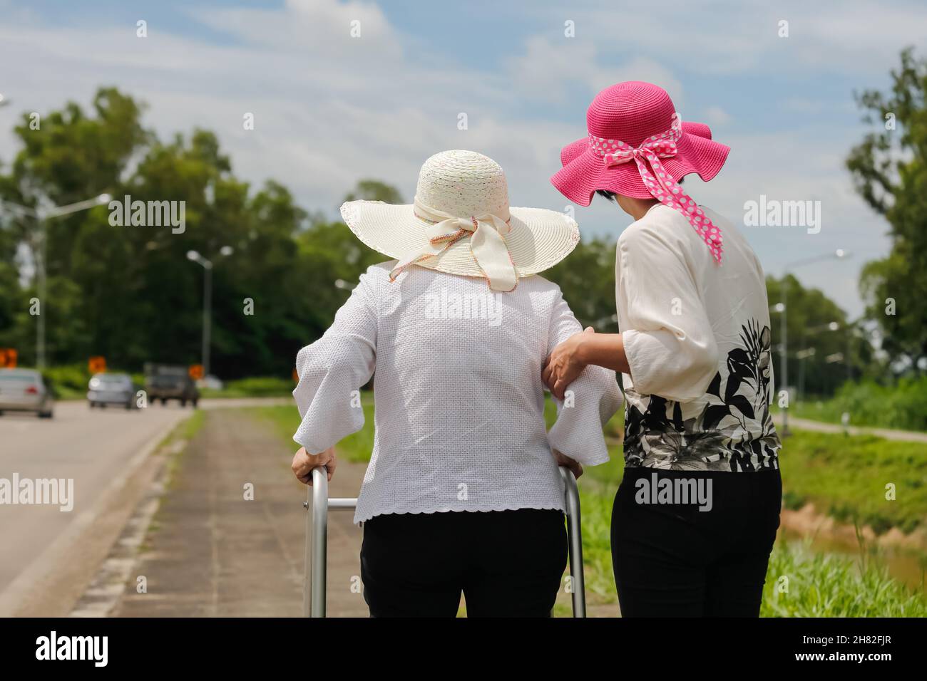 La figlia prende cura la donna anziana che cammina sulla strada in forte luce del sole. Foto Stock