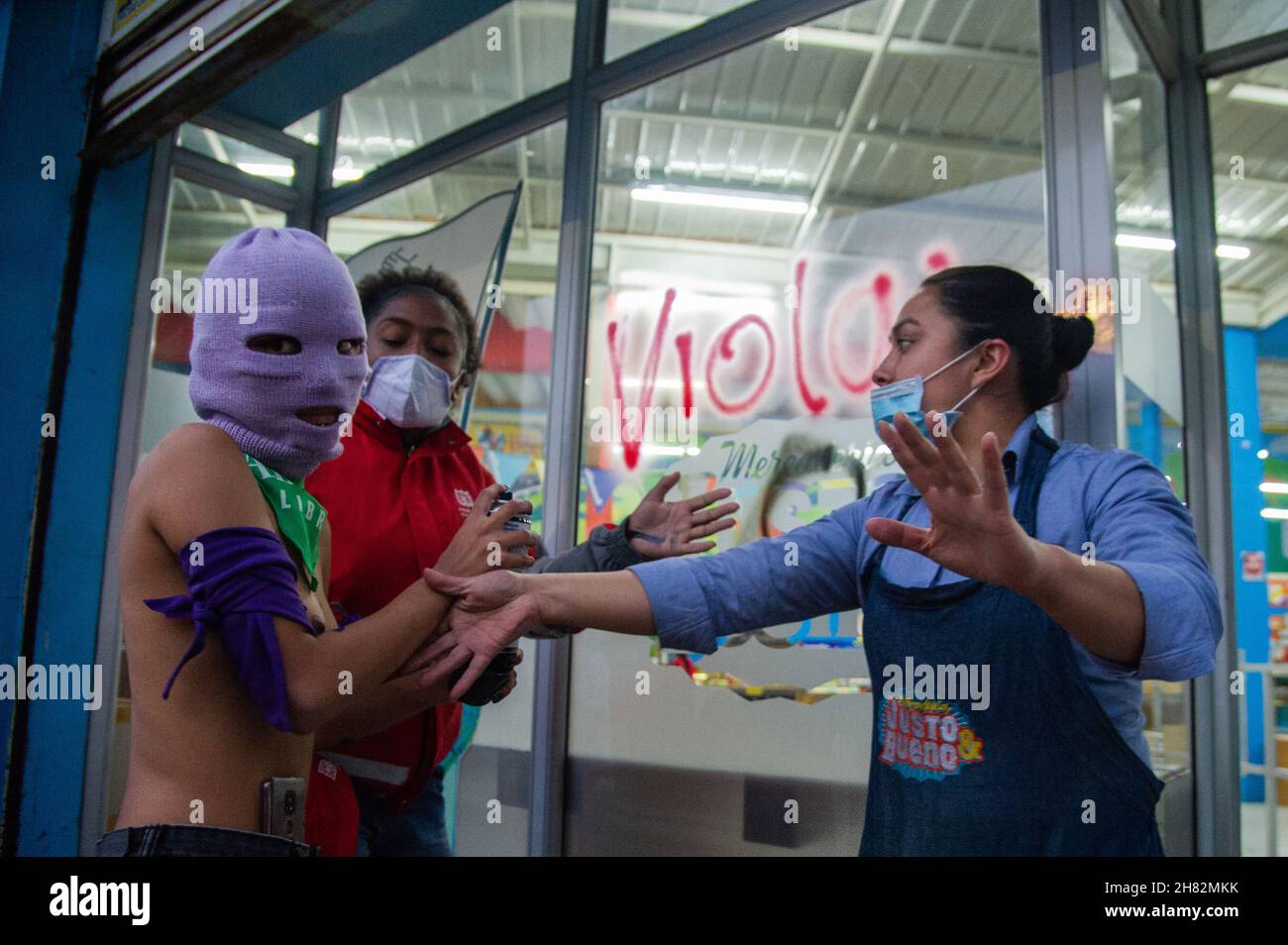 Una femminista radicale è tenuta indietro dopo aver graffiato una finestra di supermercato durante la Giornata Internazionale per l'eliminazione della violenza contro le manifestazioni femminili a Bogotà, Colombia, il 25 novembre 2021. Foto Stock