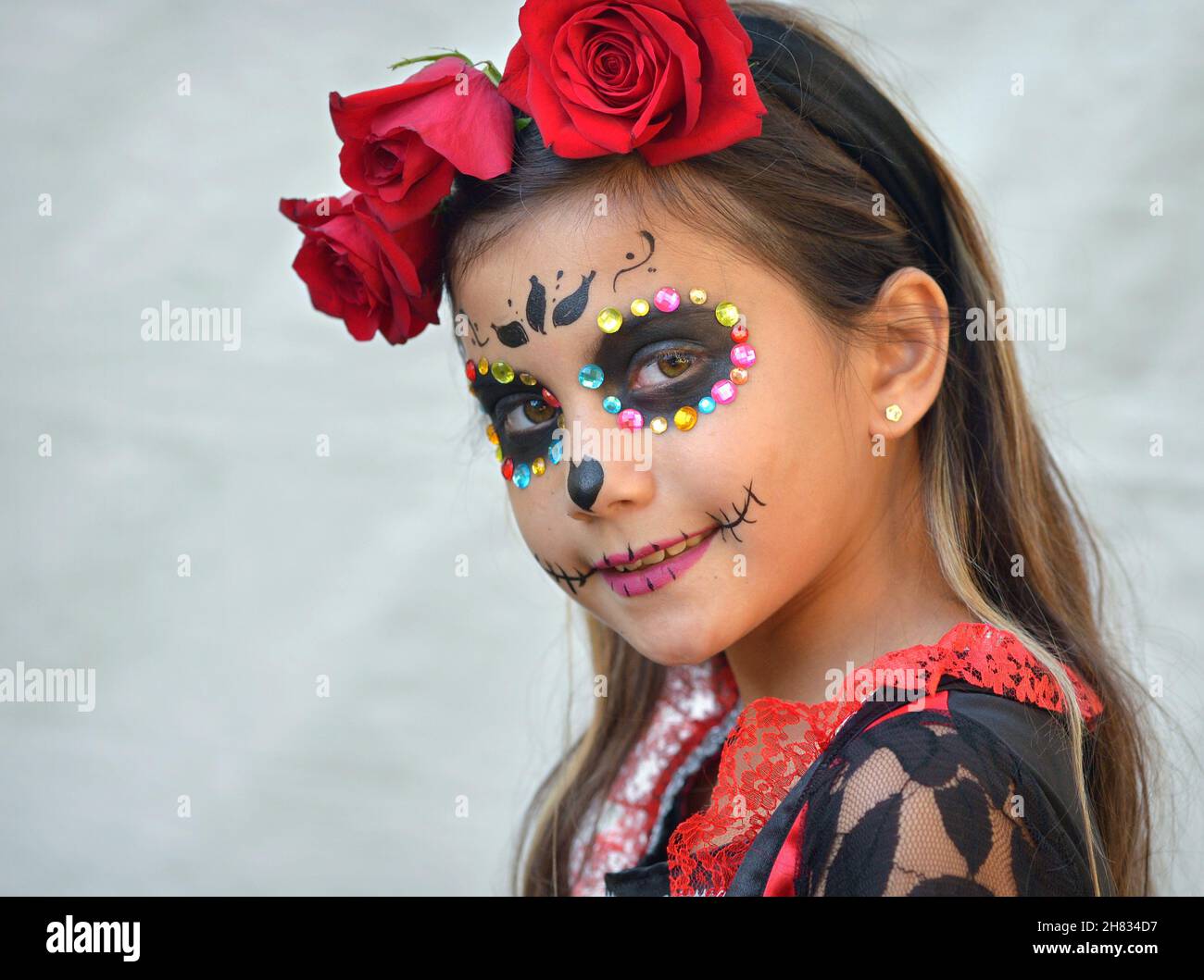 Bella ragazza pre-teen messicana Yucatecan vestita con tradizionale Catrina viso make-up e glitter viso gemme il giorno dei morti guarda lo spettatore. Foto Stock