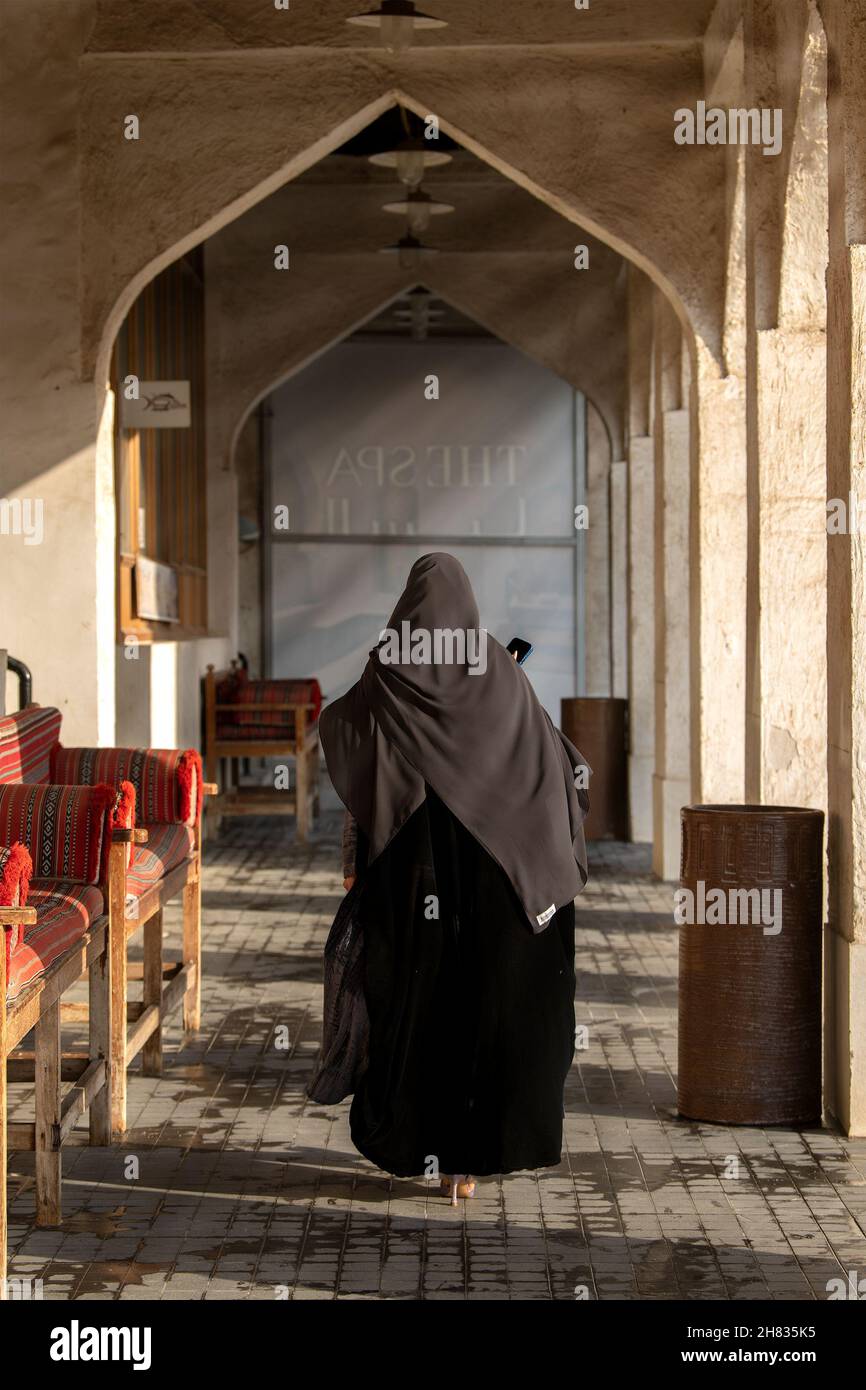 Vecchio mercato in Souq Waqif - bazaar orientale in Doha. Una signora araba che cammina nella vista posteriore del souq Foto Stock