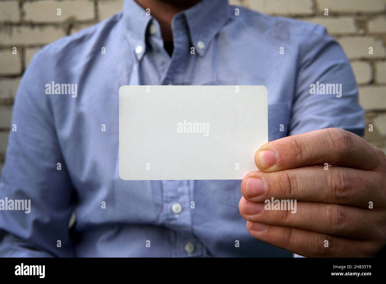 Uomo d'affari che consegna un biglietto da visita vuoto su sfondo bianco muro di mattoni sulla strada. Una carta di credito di plastica o carta da visita come mockup per i desi Foto Stock