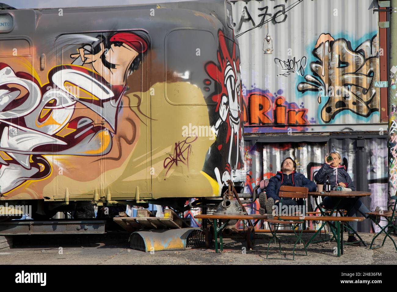 Due uomini che bevono un drink accanto ai graffiti hanno spruzzato la vecchia ferrovia nella zona del progetto culturale Bahnwaerter Thiel, Monaco, Baviera, Germania. Foto Stock