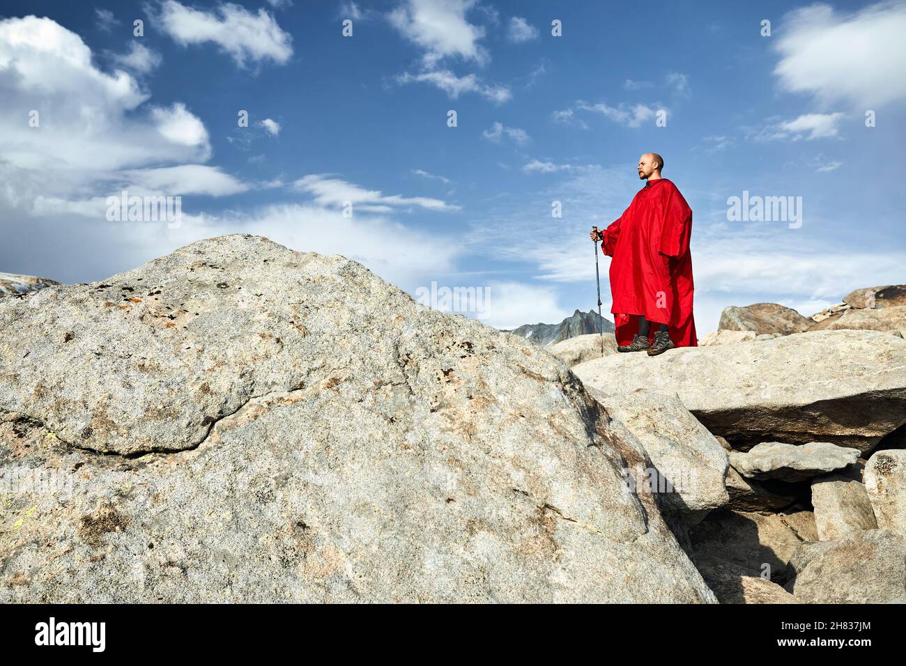 Uomo in copertura di pioggia rossa sulla roccia nelle belle montagne contro il cielo blu Foto Stock