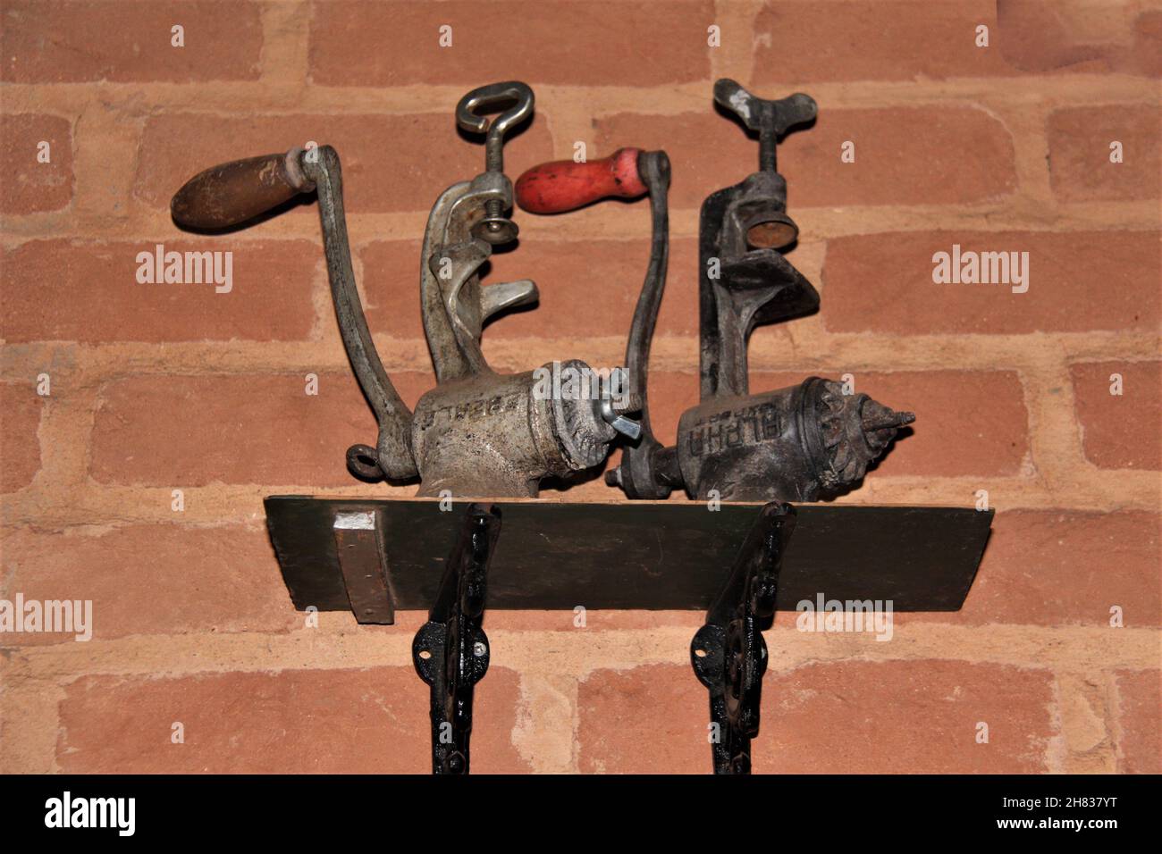 Antico macinacaffè di ferro di manovella su una mensola di legno su una parete di mattone, usato come decorazione. Foto Stock