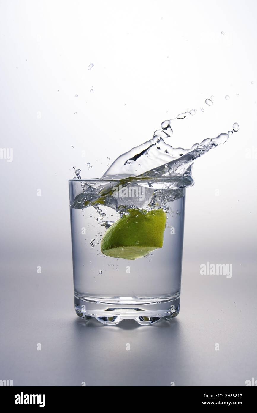Il pezzo di lime schegge in un bicchiere di liquido chiaro o acqua su una superficie grigia e sfondo bianco Foto Stock
